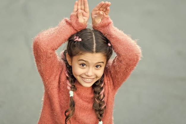 Cute bunny Happy easter Holiday bunny girl posing like rabbit grey background Child smiling play bunny role Playful baby celebrate easter Spring holidays Talent and acting Happy childhood