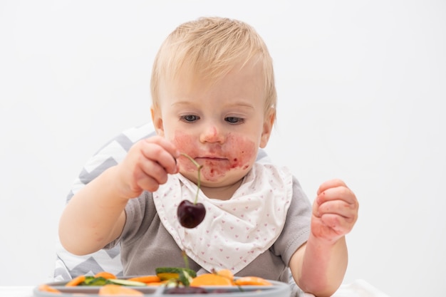 Cute caucasian baby about 1 year old eating fresh vegetables at high chair Selffeeding for kids Babyled weaning idea Healthy nutrition of solid food for infant