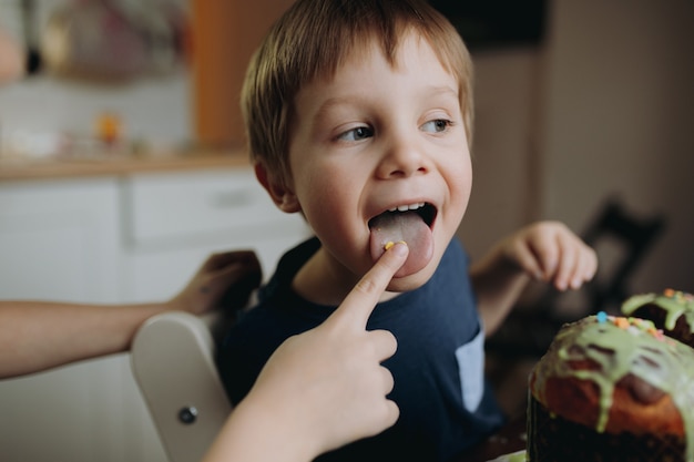 Симпатичный кавказский мальчик вкушает сахарную начинку с руками своего брата, украшая пасхальный кулич. Фото высокого качества
