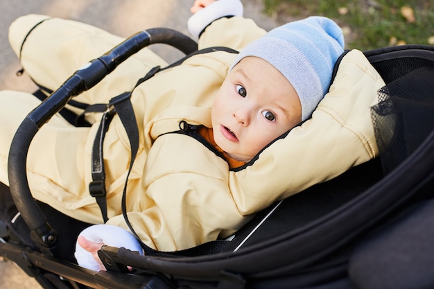 Cute Caucasian baby boy in warm clothes sits in a stroller.