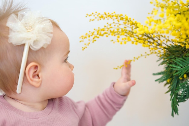 Photo cute caucasian baby girl toddler and bouquet of yellow mimosa flowers spring concept chil