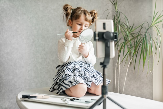 Cute caucasian baby girl video vlogger, phone on a tripod.