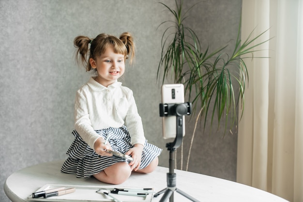 Cute caucasian baby girl video vlogger, phone on a tripod.