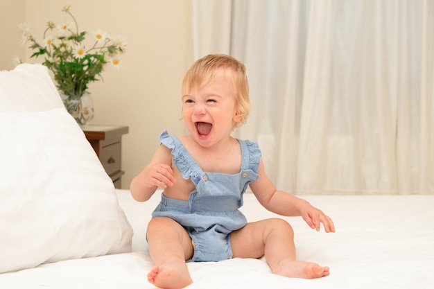 Cute caucasian blonde baby girl  playing having fun on white sheet and blanket on bed