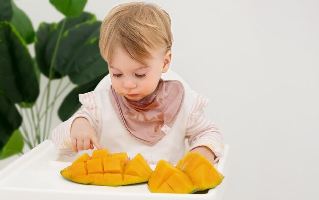 Cute caucasian blonde baby girlinfanttoddlerchild eat fresh mangoKid has lunchmealCopy space