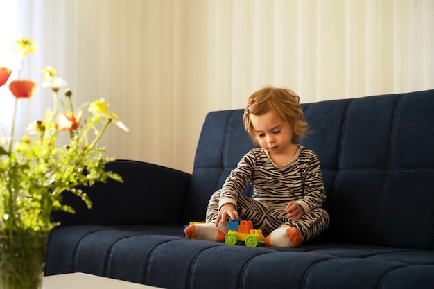 Cute caucasian blonde baby girltoddler infant adorable kid 12 years old lying on sofa playing with tinker toys in modern cozy interior at home Child having fun indoorsdevelopment game concept