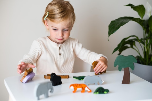 Cute caucasian blonde toddler kid child girl twothree year old playing indoor with eco safe wooden coloured toy animals on white gray backgroundEarly preschool developmentgameCrop shot