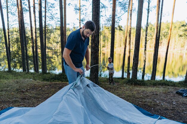 父親がテントを張るのを助けるかわいい白人の少年 家族キャンプのコンセプト