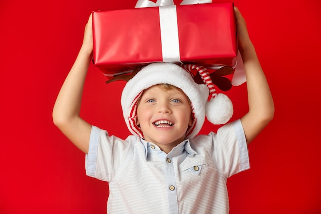 Cute Caucasian boy holds a large festive box on his head with his hands