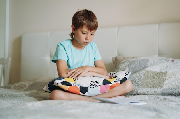 Cute caucasian boy reading a book sitting on bed in parents bedroom