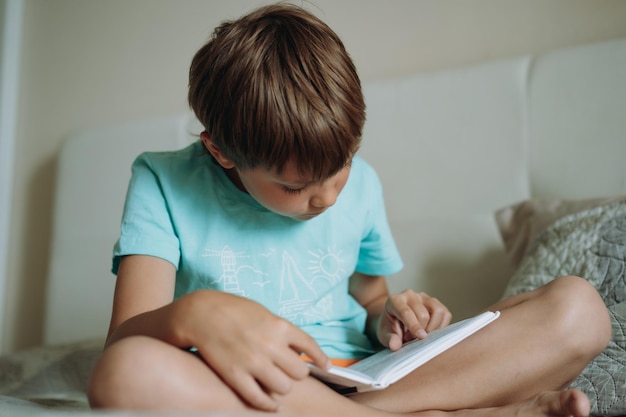 Cute caucasian boy reading a book sitting on bed in parents bedroom