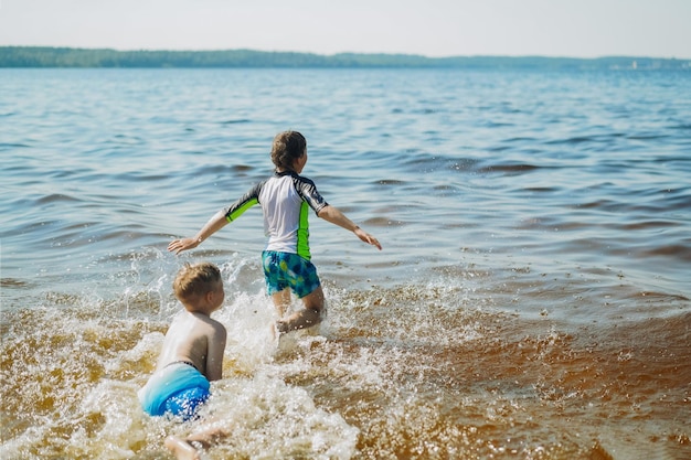 水しぶきと笑いで水に走っているかわいい白人の少年 海辺での休暇