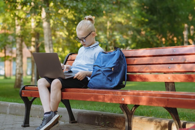 Cute caucasian boy sitting on bench in park with laptop computer Black screen