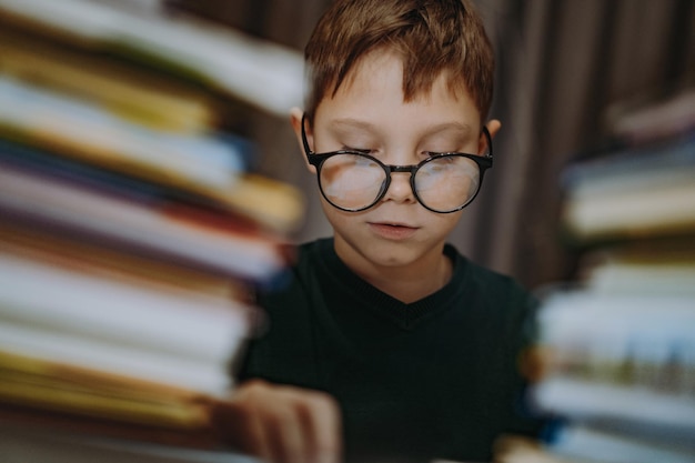 Cute caucasian boy wearing glasses covering head with book cheerful boy peeking from behind piles of...