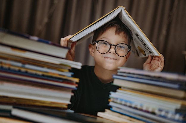 眼鏡をかけて頭を覆っているかわいい白人の少年と本の陽気な少年が山の後ろから覗いています...