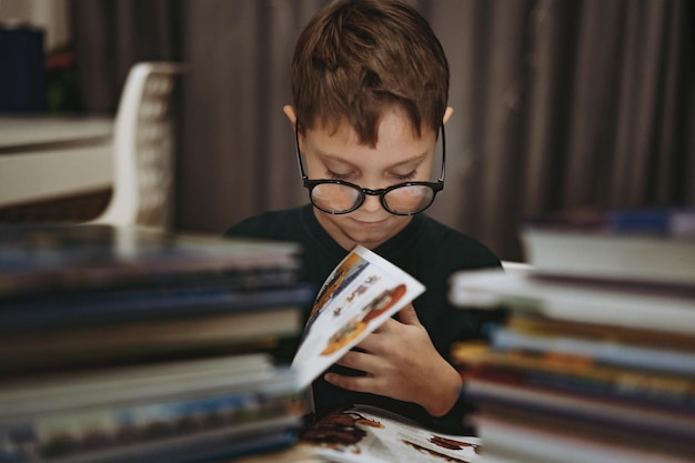 Cute caucasian boy wearing glasses reading a book Cheerful boy peeking from behind piles of books