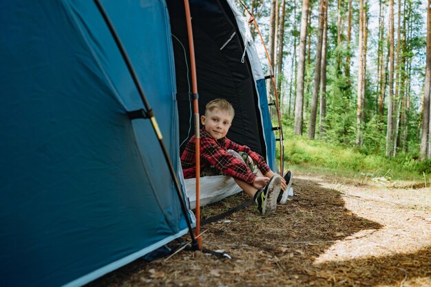 Cute caucasian boy wearing hat sitting inside a big touristic tent family camping concept