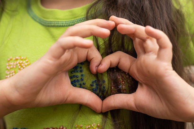 A cute Caucasian child holds a palm in the shape of a heart.