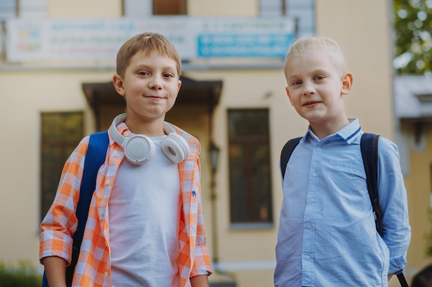 Cute caucasian children before school with backpacks on sunny day Begining of academic year Boys by school doorstep