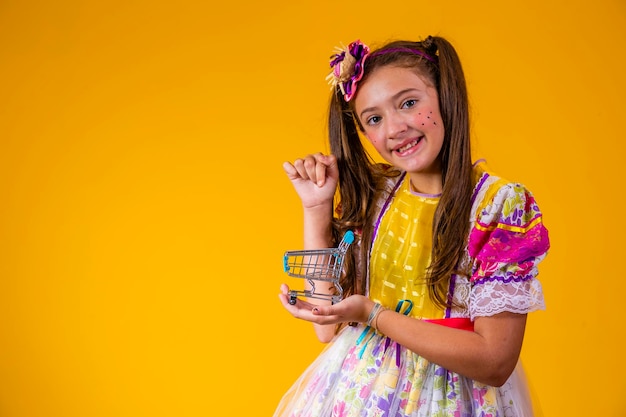 Cute caucasian girl in festa junina outfit holding a mini shopping cart concept of ecommerce and festa junina