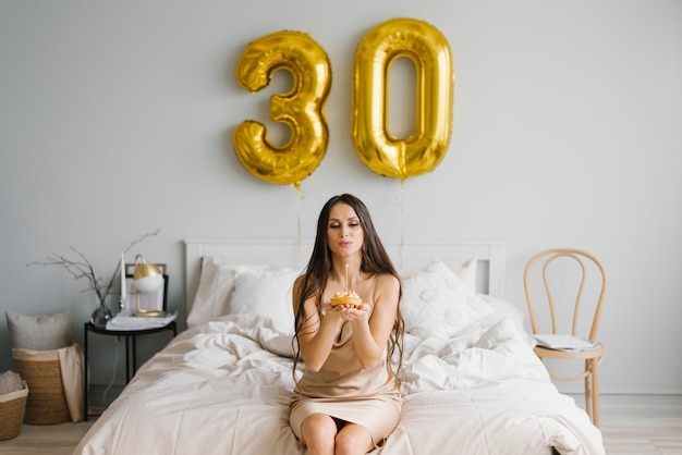 Cute Caucasian girl in a nightgown who is congratulated on her birthday in bed blows out a candle on a cake and makes a wish for a celebration lifestyle and holiday concept