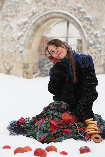 写真 ベーグルと赤いリンゴと雪の中で座っているかわいい白人の女の子