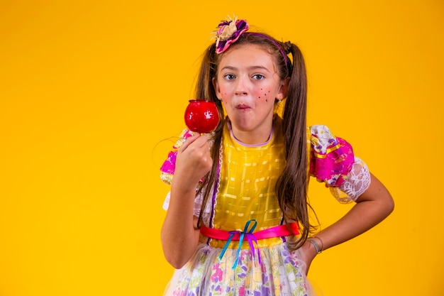 Cute caucasian girl in typical festa junina outfit eating apple with caramel