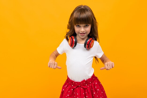 Cute caucasian girl with red headphones on a yellow wall