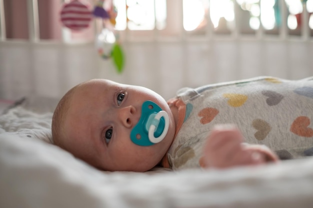 Cute caucasian little baby with pacifier resting in bed