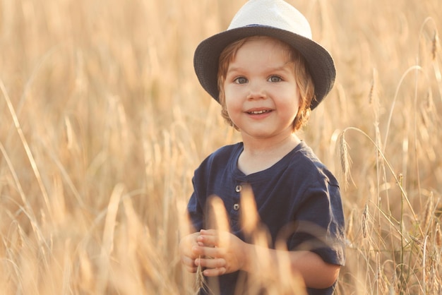 Cute caucasian little boy 3 years old on a straw hat walking in a wheat field on summer day