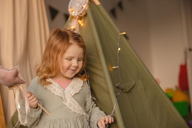 Cute caucasian little girl child with red hair wears green dress at home playing with toys Baby concept