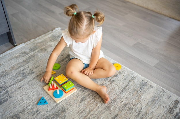 家の床でエコ木のおもちゃで遊ぶかわいい白人の女の子 モンテッソーリのおもちゃ 教育的なゲームをしている子供