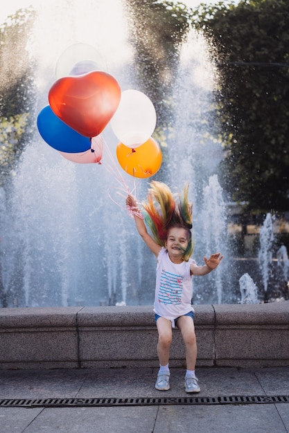 cute caucasian smiling girl with colorful dyed hair holding baloons jumping from fountain