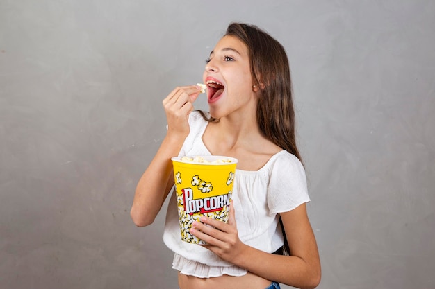 Cute caucasian teenage girl eating popcorn on neutral background with free space for text Holiday entertainment concept girl eating popcorn