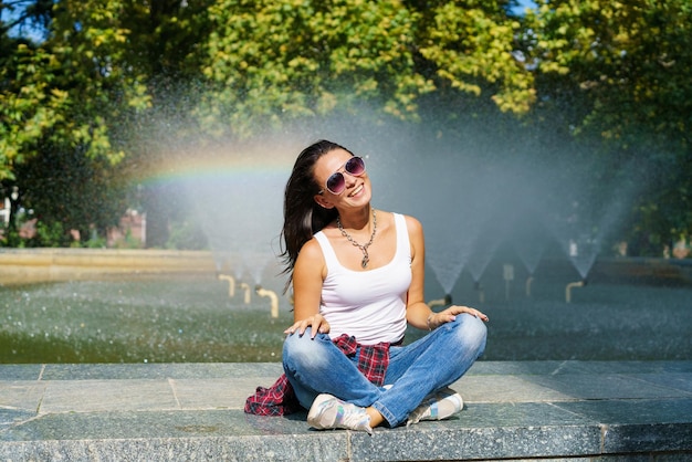 Cute caucasian woman sits by fountain in park on sunny day enjoys the coolness