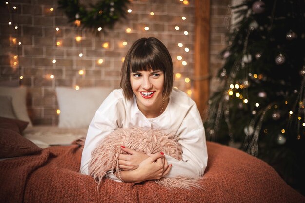 Cute caucasian woman sitting on sofa in new year. Indoor portrait of confident girl posing near christmas tree. Soft focus. Selective focus.