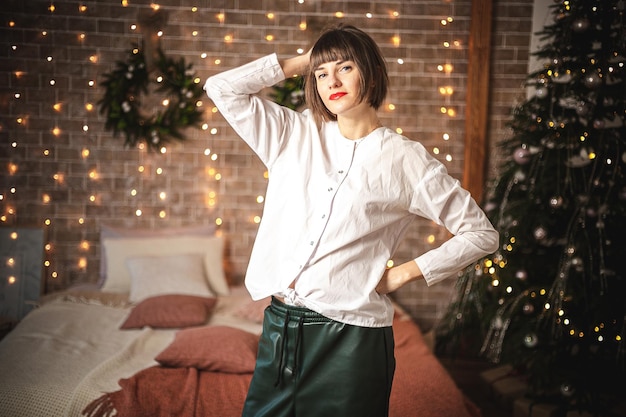 Cute caucasian woman standing near the sofa in new year. Indoor portrait of confident girl posing near christmas tree. Soft focus. Selective focus.