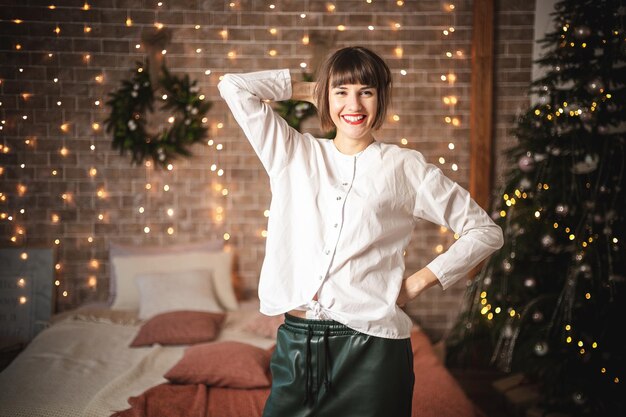 Cute caucasian woman standing near the sofa in new year. Indoor portrait of confident girl posing near christmas tree. Soft focus. Selective focus.