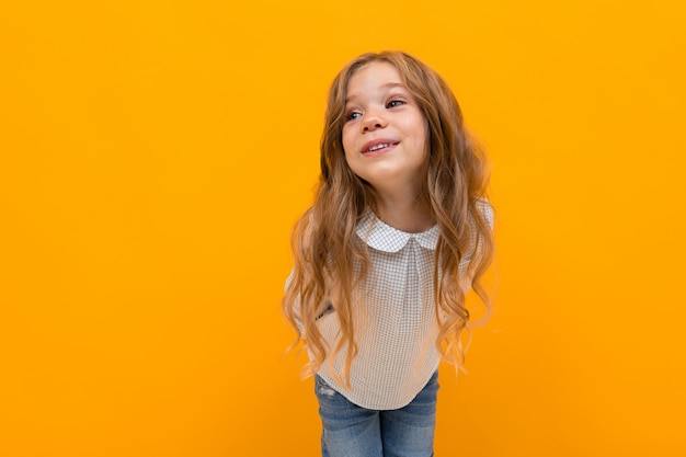 Cute charming girl child with long hair posing on yellow with copy space