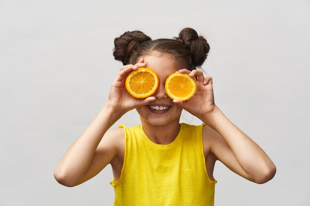 Cute charming girl in yellow t-shirt, laughing merrily and holding half orange.