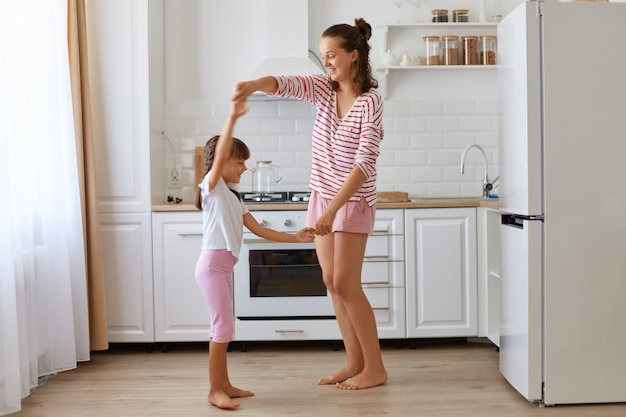 Cute charming little girl dancing with mother, r feeling
amazing dancing with her loving mommy, expressing happiness and
positive emotions, family having fun at home.