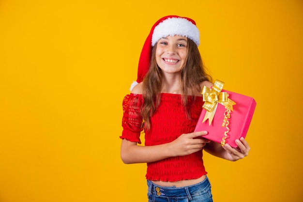 Cute cheerful girl in a Christmas hat on a colored background holding a gift