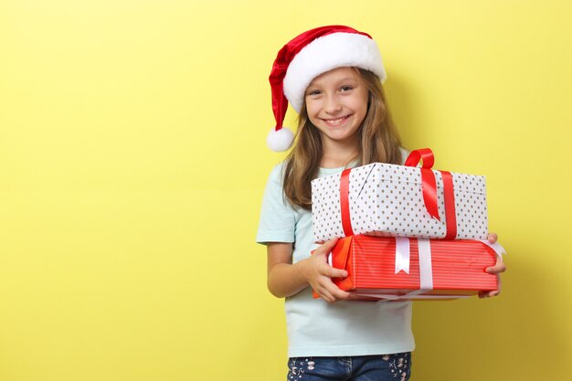 Cute cheerful girl in a christmas hat on a colored background holding a gift