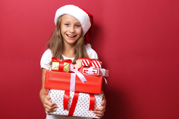 Cute cheerful girl in a christmas hat on a colored background holding a gift