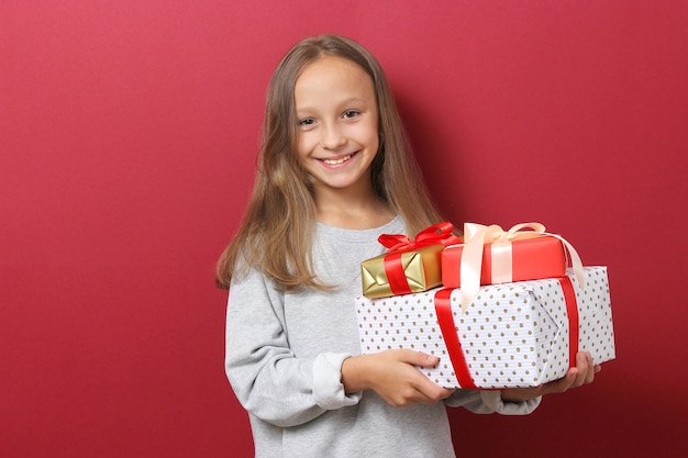 Cute cheerful girl in a christmas hat on a colored background holding a gift