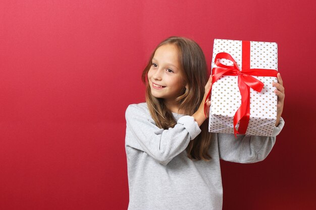 Cute cheerful girl in a christmas hat on a colored background holding a gift