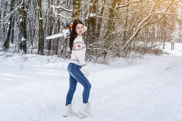 かわいい陽気な女の子はチェーンソーで森の中で雪の中を行く 森林伐採伐採