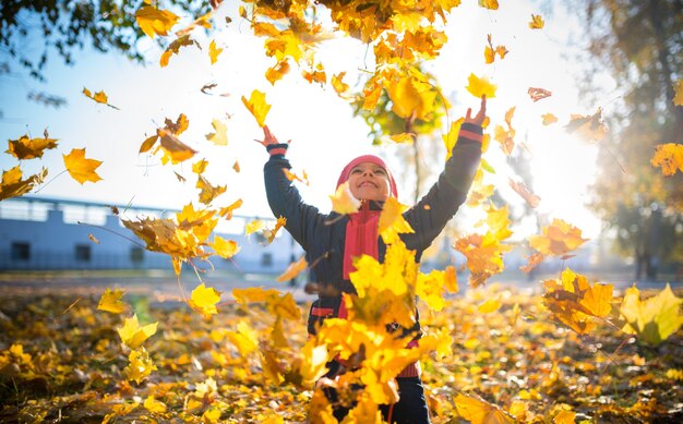 Cute cheerful girl throws up yellow maple leaves