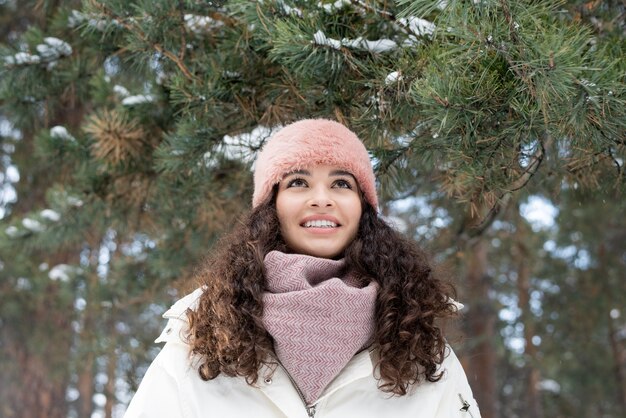 Cute cheerful girl in warm winterwear enjoying winter day in the forest or park while chilling out at leisure