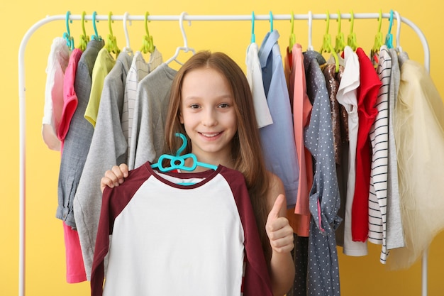 Cute cheerful little girl chooses clothes with floor hangers